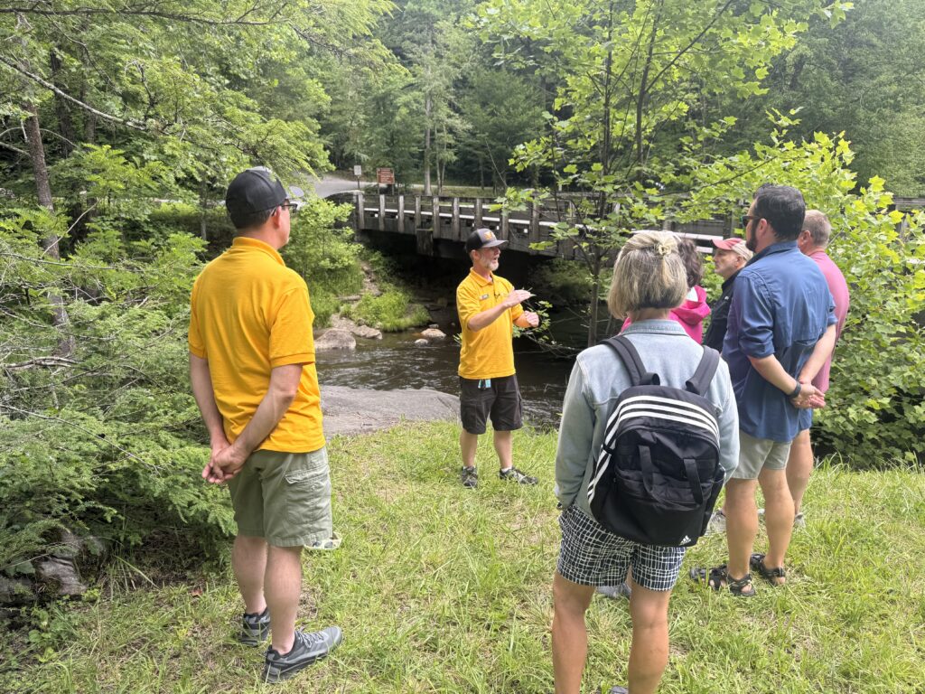 Luke Wayne of Canyon Ministries teaching guests beside a forest stream and bridge in Great Smoky Mountains National Park
